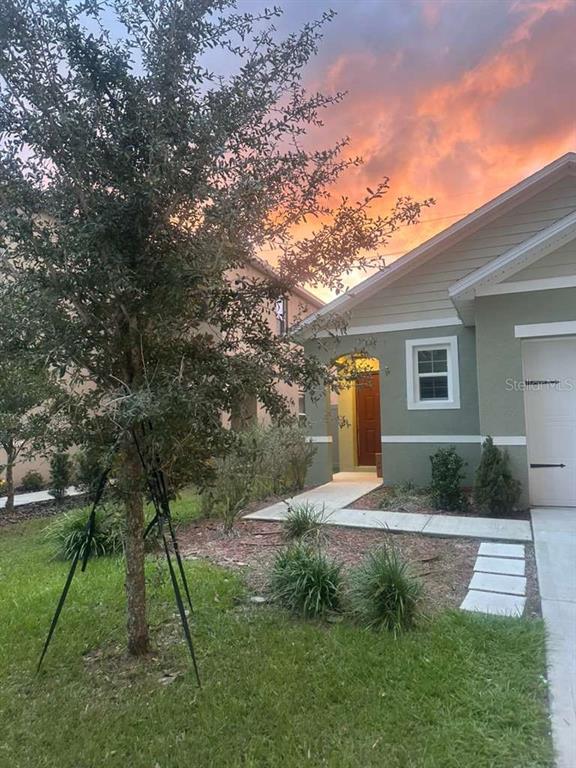 A green house exterior with a wooden front door and a sunset in the sky — 336 GINA LANE, DAVENPORT, FL