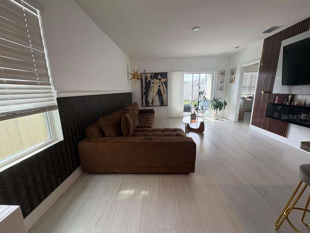 A living room features a brown sectional sofa, wood-slat wall accents, and light-colored flooring — 336 GINA LANE, DAVENPORT, FL
