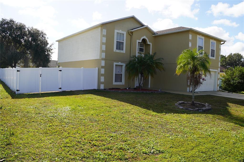 A two-story house with tan stucco, white trim, and a white vinyl privacy fence — 304 COCOA COURT, KISSIMMEE, FL