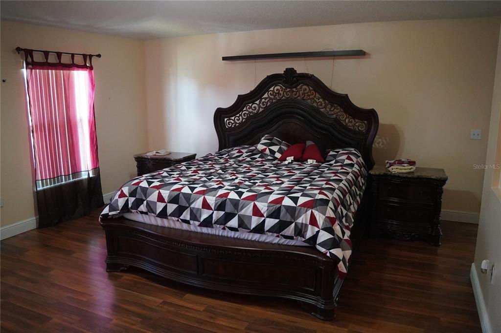 A bedroom features a large dark wood bed frame, patterned bedding, and dark wood flooring — 304 COCOA COURT, KISSIMMEE, FL