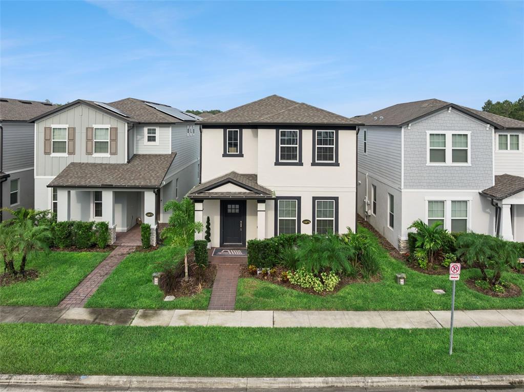 A two-story house with a beige stucco exterior and dark trim sits between two neighboring homes — 13879 LANYARD WAY, WINTER GARDEN, FL