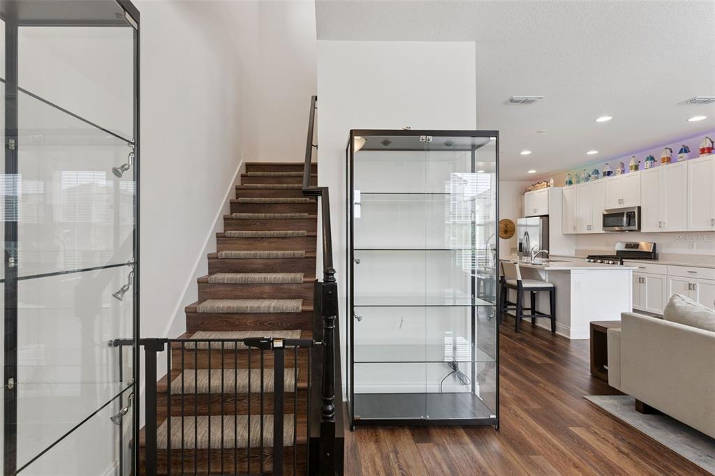 A staircase with a safety gate sits beside a glass display cabinet in an open-concept home — 13879 LANYARD WAY, WINTER GARDEN, FL