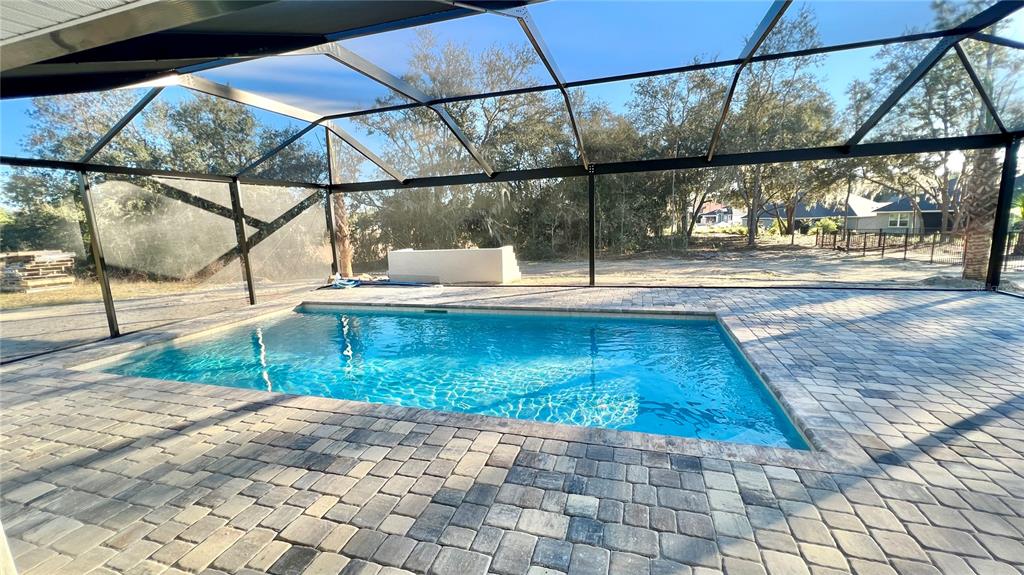 A rectangular swimming pool sits on a paved patio inside a screened-in pool enclosure — 17920 SW 66TH PLACE, DUNNELLON, FL