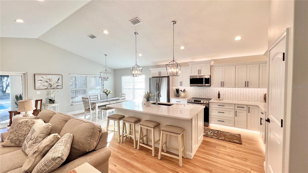 A bright, open-concept kitchen features a large white island, light wood floors, and pendant lighting — 17920 SW 66TH PLACE, DUNNELLON, FL