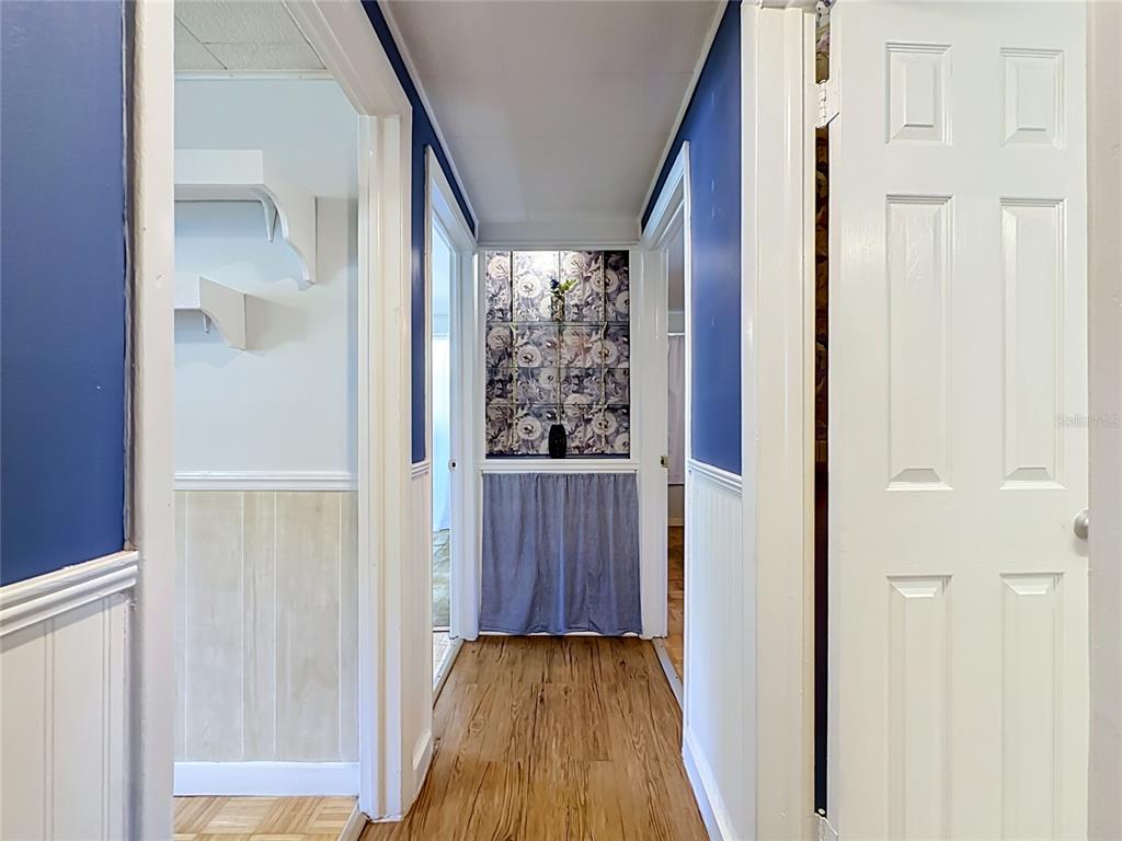 A hallway with blue walls, white wainscoting, wood-look flooring, and a floral-patterned accent wall — 10131 AGAVE ROAD, JACKSONVILLE, FL