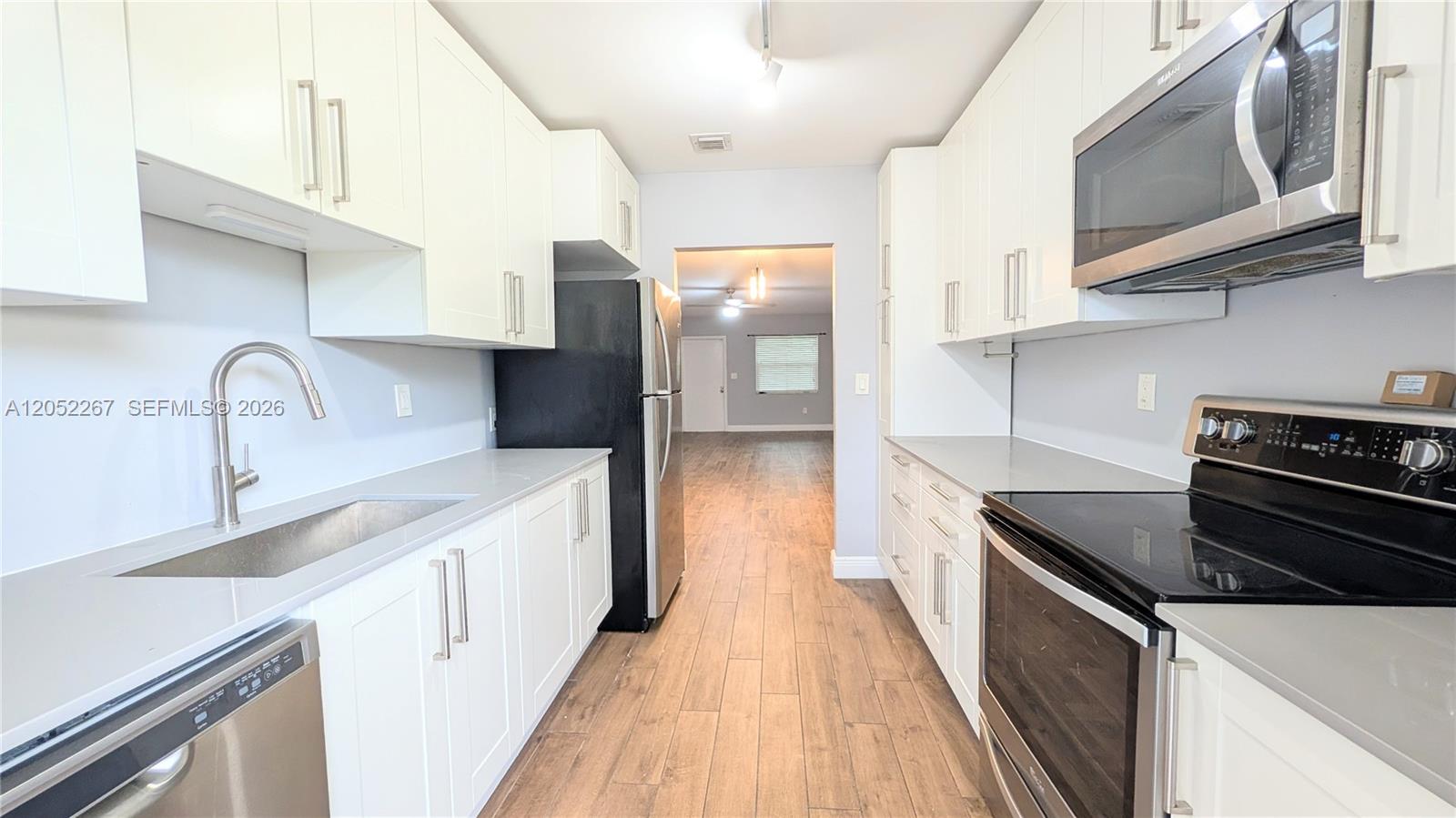 A galley kitchen features white cabinets, stainless steel appliances, and wood-look tile flooring — 315 SE 23rd Ave # 5, Pompano Beach FL 33062, POMPANO BEACH, FL