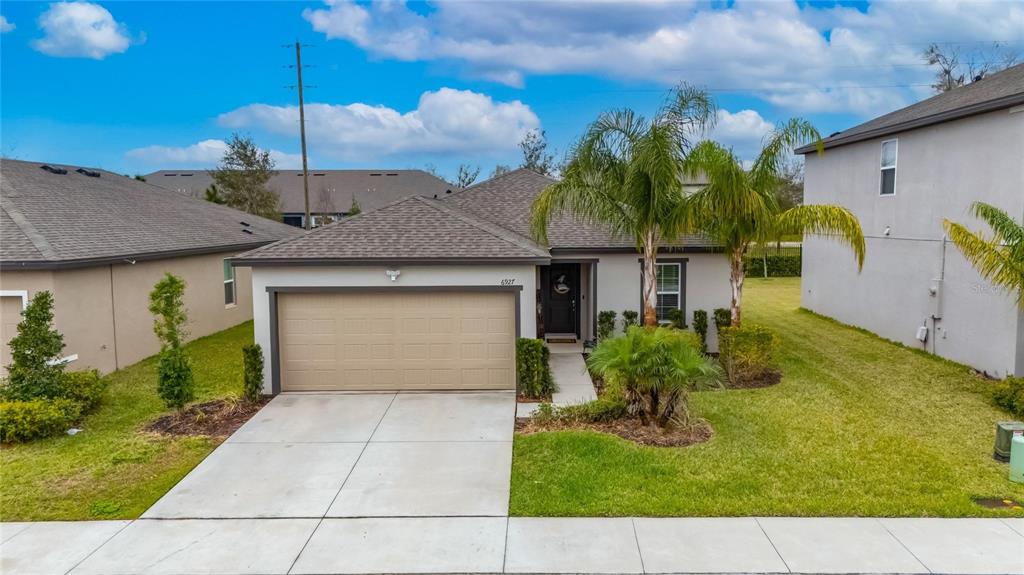 A single-story house with a tan garage, gray roof, and palm trees in the front yard — 6927 SHELBY LYNN WAY, ZEPHYRHILLS, FL