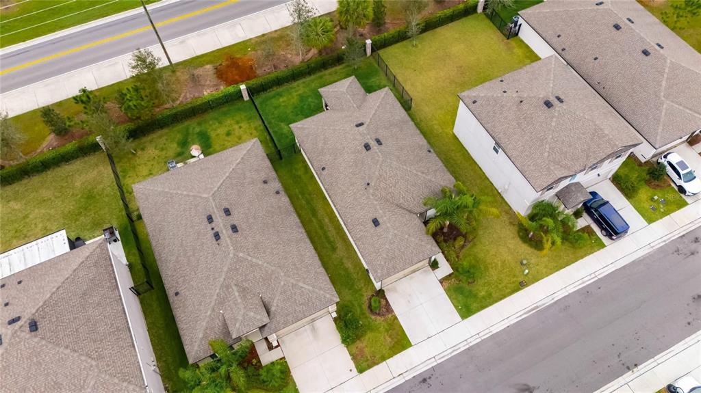 An aerial view shows three suburban houses with gray shingled roofs and concrete driveways — 6927 SHELBY LYNN WAY, ZEPHYRHILLS, FL