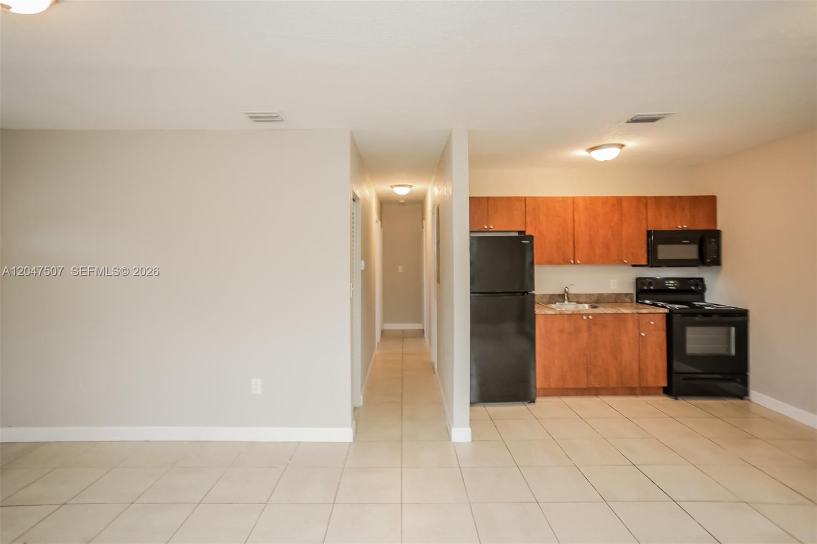 This room features a kitchen with wood cabinets and black appliances next to a hallway — 14640 Tyler St, Miami FL 33176, MIAMI, FL