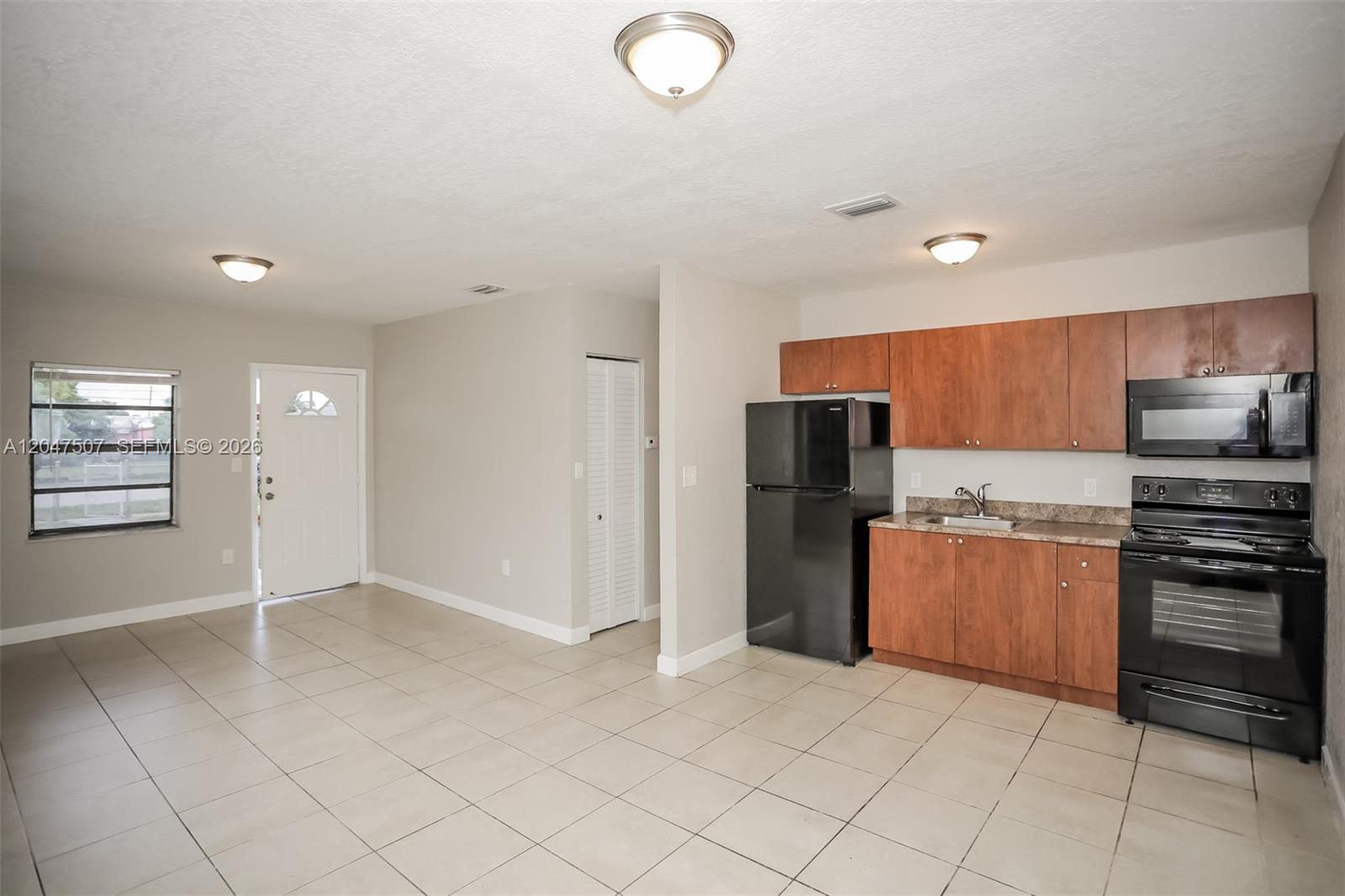 A kitchen with wood cabinets and black appliances opens into a tiled living area — 14640 Tyler St, Miami FL 33176, MIAMI, FL