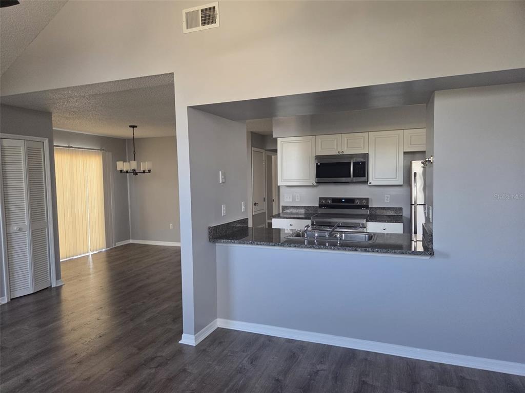A living room with wood-look flooring opens to a kitchen featuring white cabinets and stainless appliances — 3226 FOX SQUIRREL DRIVE, KISSIMMEE, FL