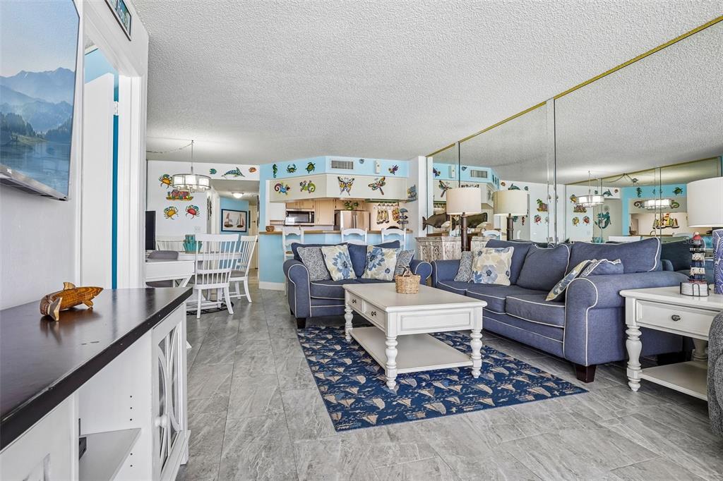 A living room features blue sofas, a coffee table, a patterned rug, and mirrored walls — 3115 S ATLANTIC AVENUE UNIT G030, DAYTONA BEACH, FL