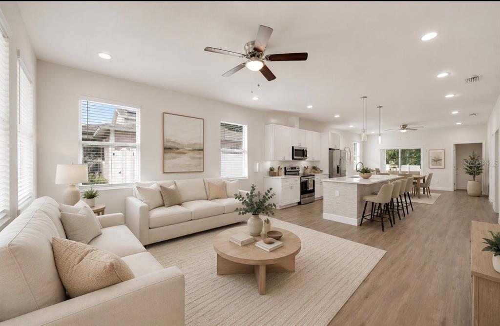 An open-concept living room and kitchen featuring light wood flooring, white cabinetry, and neutral furniture — 3706 WIGGINS LEAF STREET, TAMPA, FL