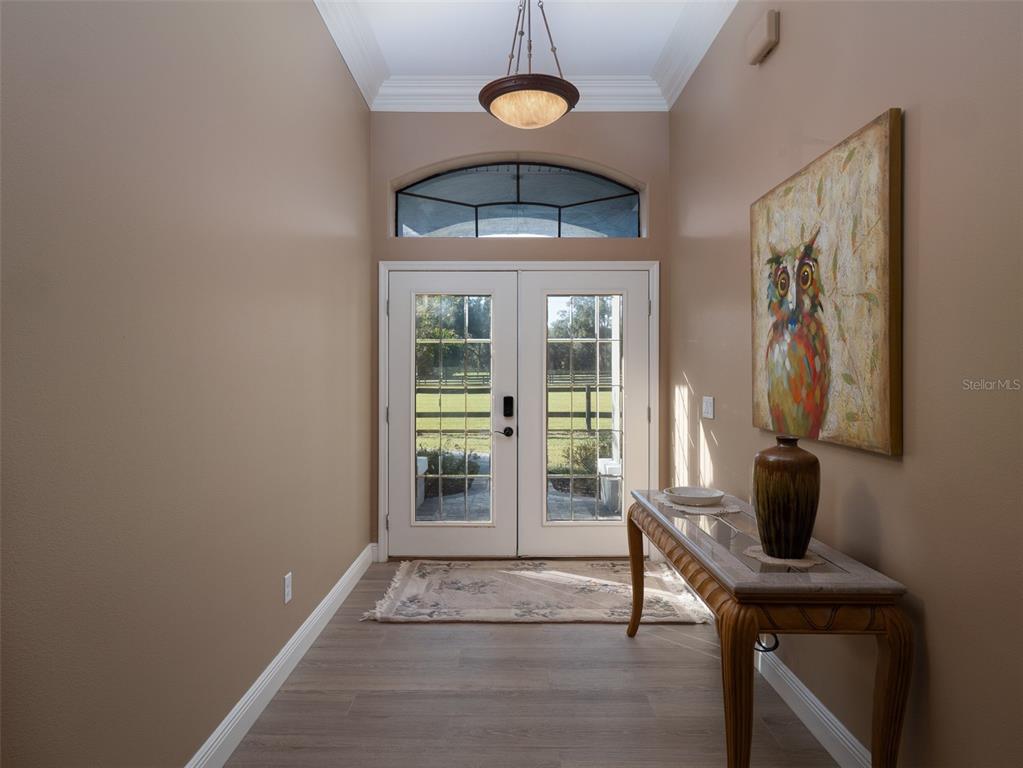 A foyer with light wood-look flooring, a console table, and double glass entry doors — 15921 NW HIGHWAY 464B, MORRISTON, FL
