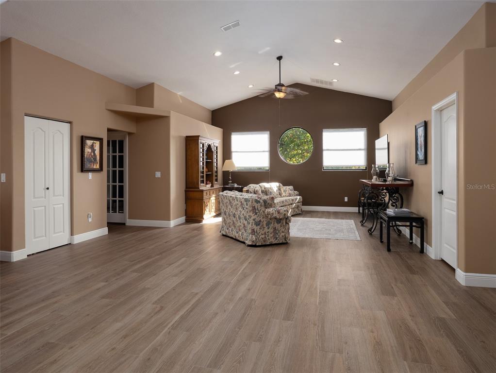 A living room features light wood-look flooring, a vaulted ceiling, and a circular accent window — 15921 NW HIGHWAY 464B, MORRISTON, FL