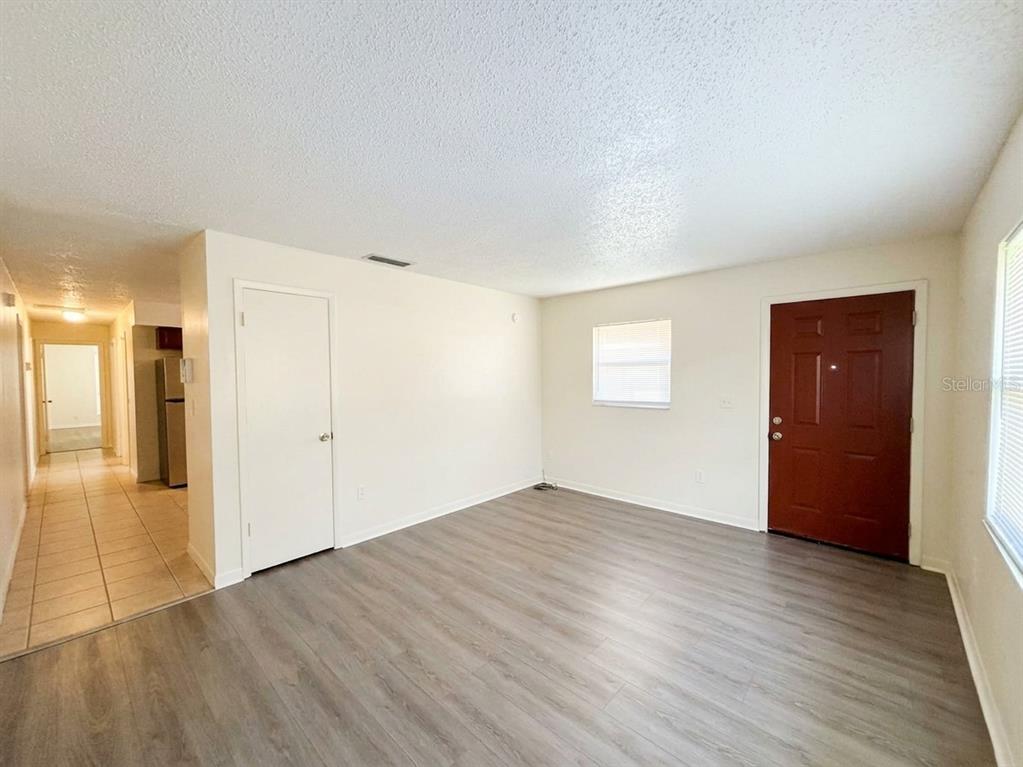 An empty room features light wood-look flooring, white walls, a brown door, and a hallway — 1236 JOSEPHINE STREET, LAKELAND, FL
