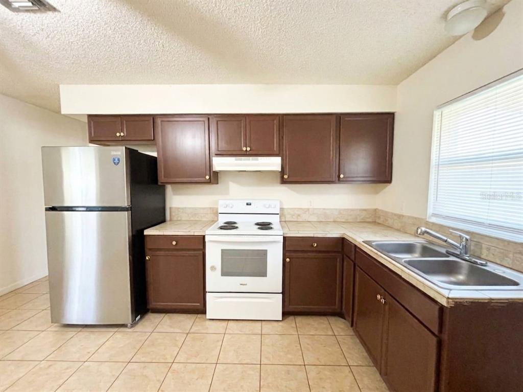 A kitchen features brown cabinets, white appliances, a stainless steel refrigerator, and tiled countertops — 1236 JOSEPHINE STREET, LAKELAND, FL