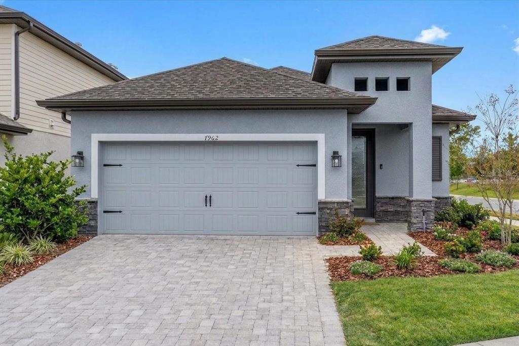 A single-story house with a gray stucco exterior, stone accents, and a paved driveway — 7962 RUMNEY LANE, REUNION, FL