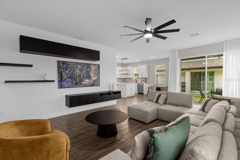 A modern living room features dark floating cabinetry, a sectional sofa, and an open kitchen — 7962 RUMNEY LANE, REUNION, FL