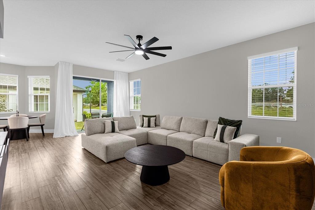 A living room features a large sectional sofa, a round coffee table, and wood flooring — 7962 RUMNEY LANE, REUNION, FL