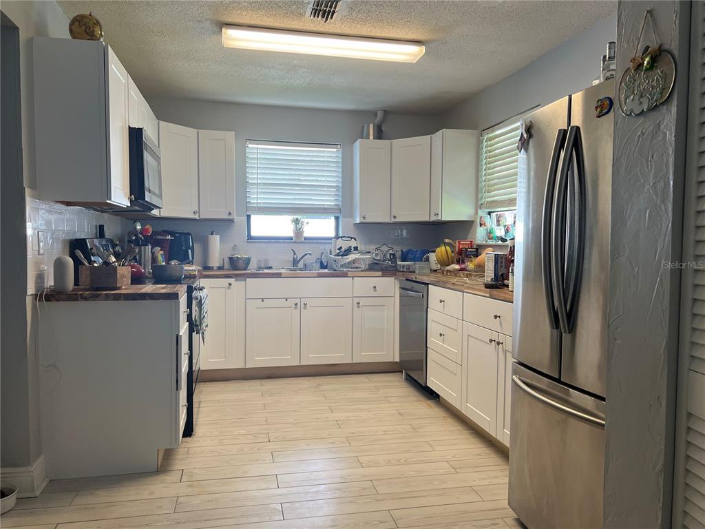 A kitchen features white cabinets, stainless steel appliances, wood countertops, and light-colored wood-look flooring — 400 PALM AVENUE, ORMOND BEACH, FL