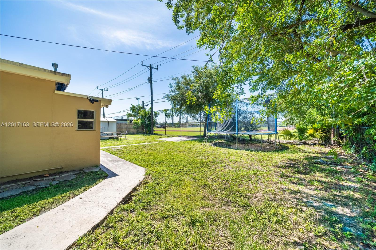 A backyard features a concrete walkway, a trampoline, and a view of a baseball field — 6472 Pierce St, Hollywood FL 33024, HOLLYWOOD, FL