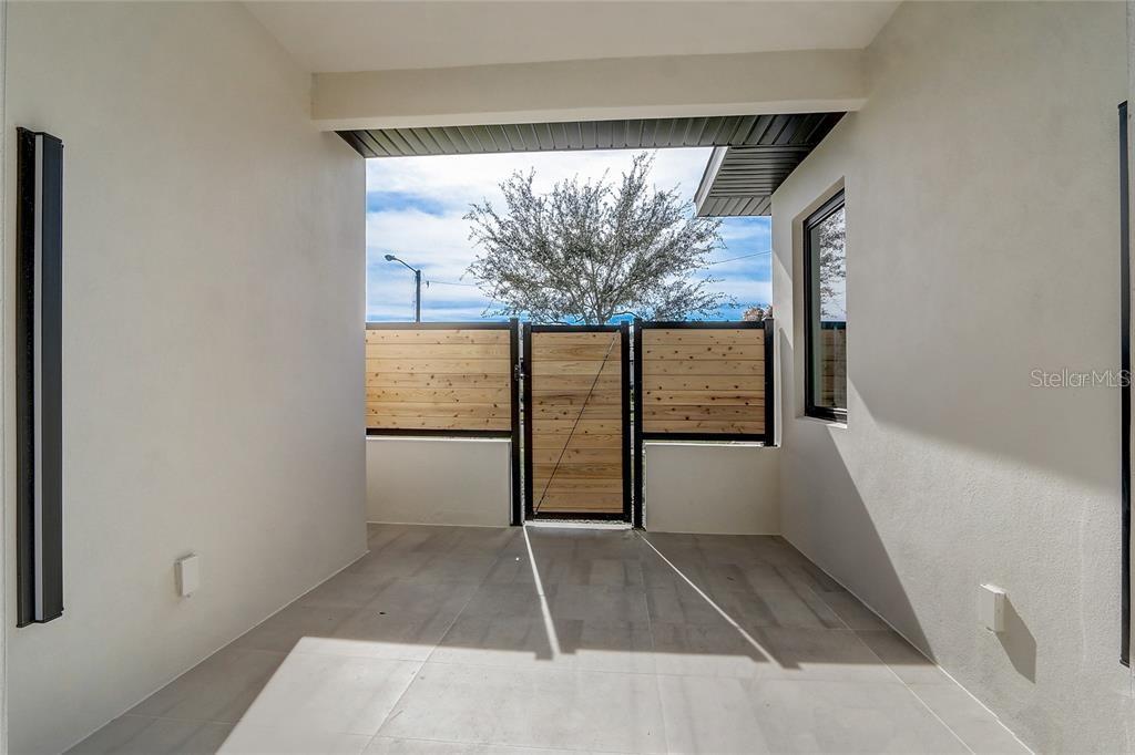 A covered patio features light-colored tile flooring, smooth white walls, and a wooden privacy gate — 641 NORTHWOOD CIRCLE, WINTER PARK, FL
