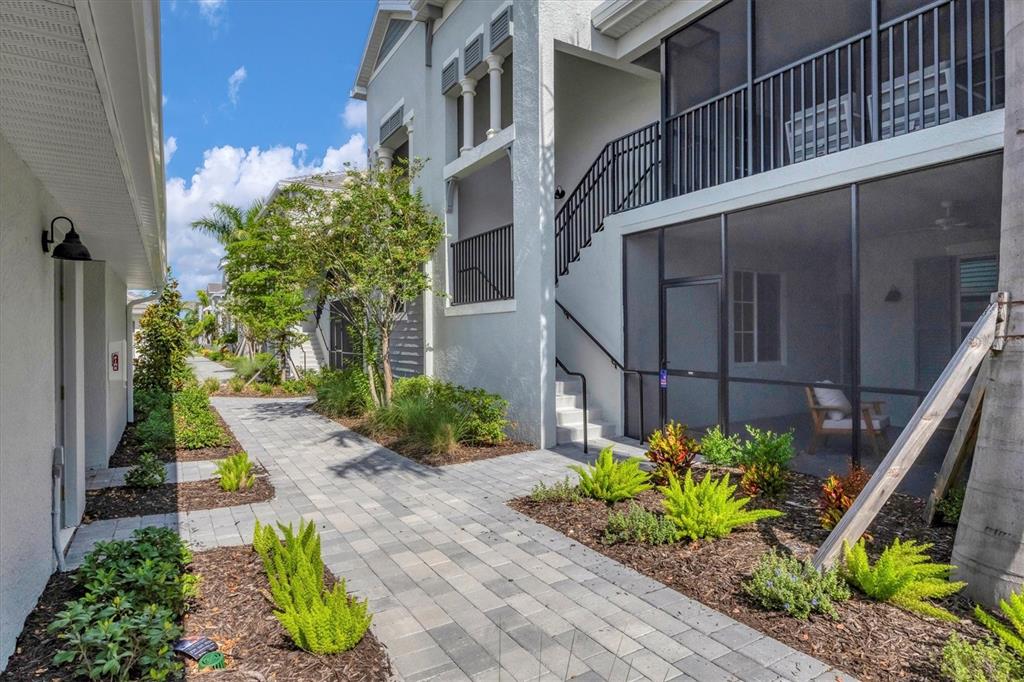 A paved walkway leads between two multi-story residential buildings with screened-in porches and landscaping — 12390 WELLEN GOLF STREET UNIT 106, VENICE, FL