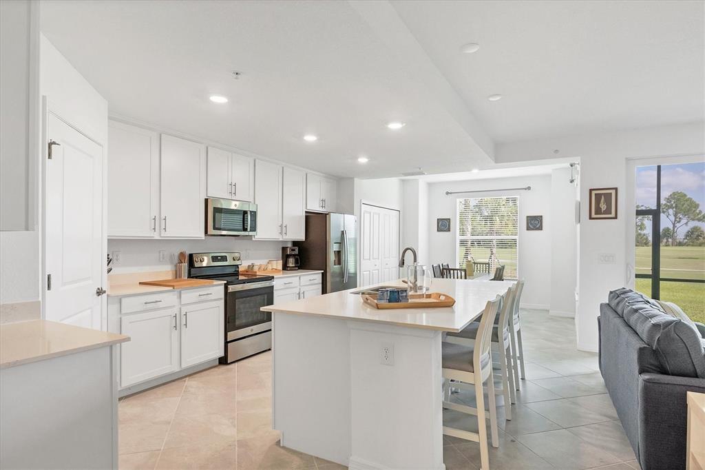A bright kitchen features white cabinets, a central island with seating, and a view outdoors — 12390 WELLEN GOLF STREET UNIT 106, VENICE, FL