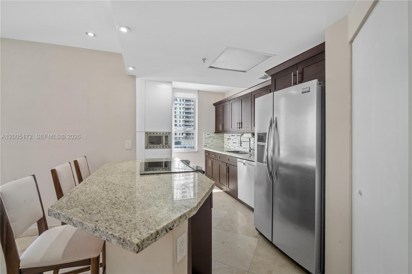 A kitchen features dark wood cabinets, granite countertops, a stainless steel refrigerator, and an island — 701 Brickell Key Blvd # 710, Miami FL 33131, MIAMI, FL