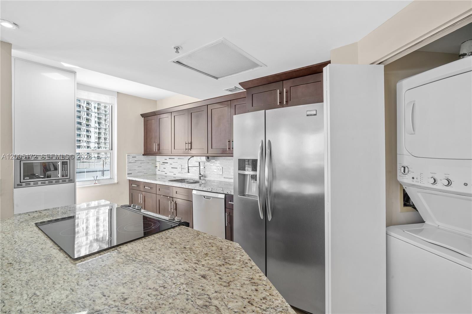 A kitchen features dark wood cabinets, granite countertops, stainless steel appliances, and a stacked washer-dryer — 701 Brickell Key Blvd # 710, Miami FL 33131, MIAMI, FL