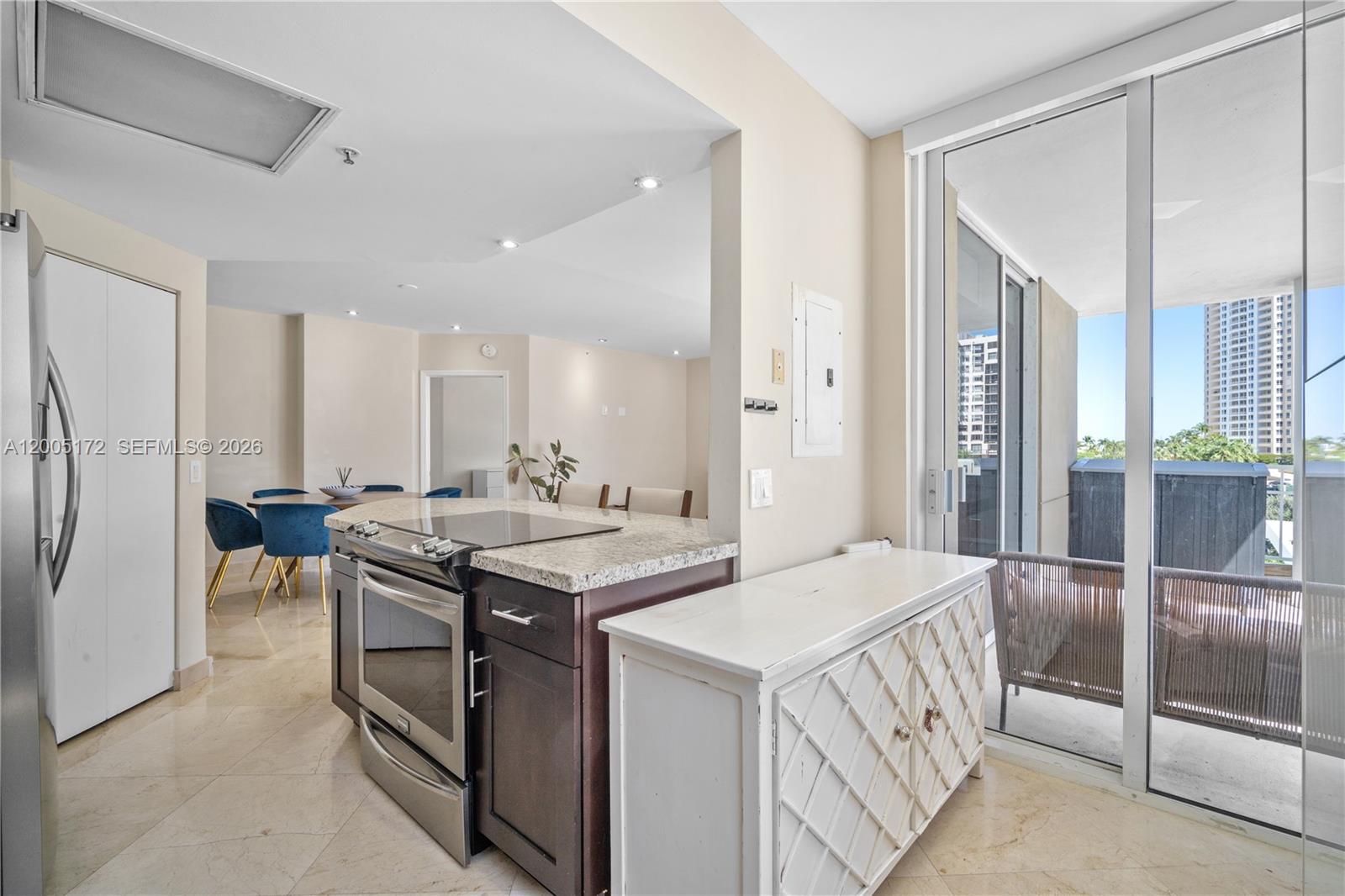 A kitchen with dark cabinets and granite countertops opens to a dining area and balcony — 701 Brickell Key Blvd # 710, Miami FL 33131, MIAMI, FL