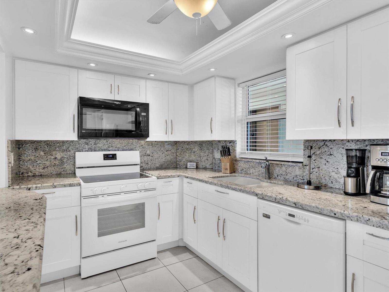 A kitchen with white cabinets, granite countertops, and white appliances under a tray ceiling — 303 N Riverside Drive # 503, Pompano Beach FL 33062, POMPANO BEACH, FL