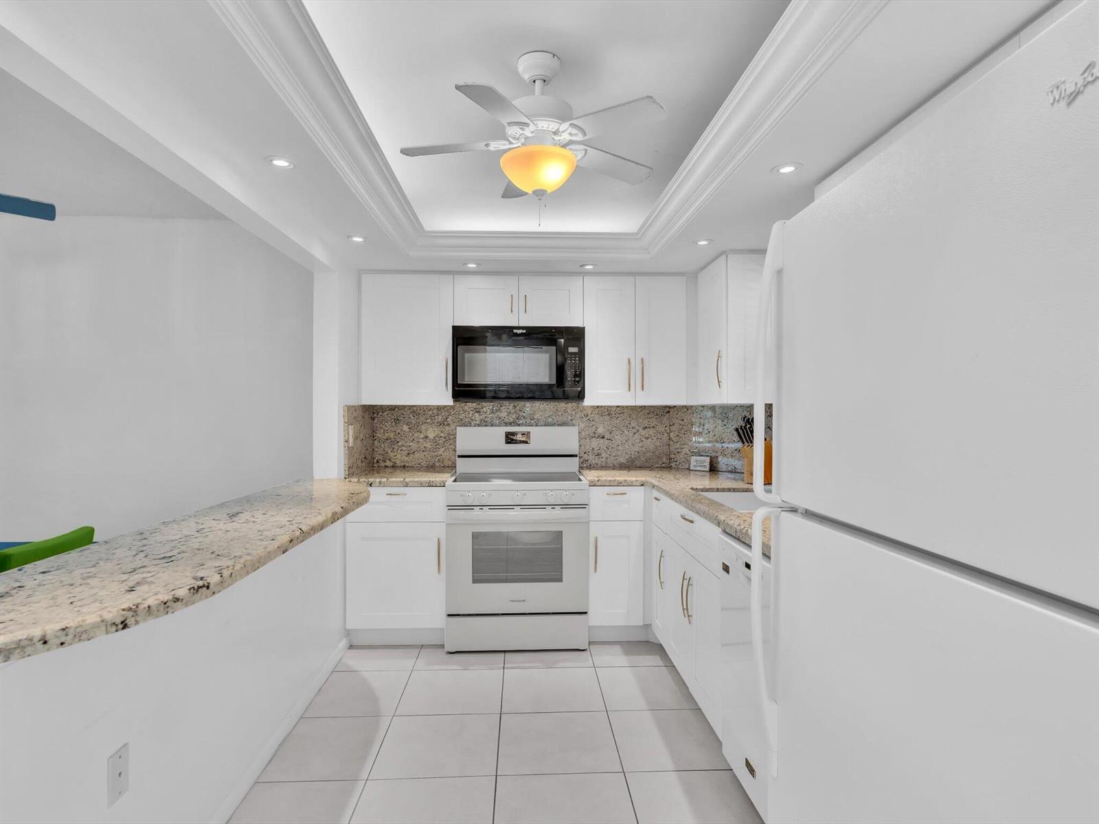 A white kitchen features granite countertops, white cabinetry, a ceiling fan, and stainless steel appliances — 303 N Riverside Drive # 503, Pompano Beach FL 33062, POMPANO BEACH, FL