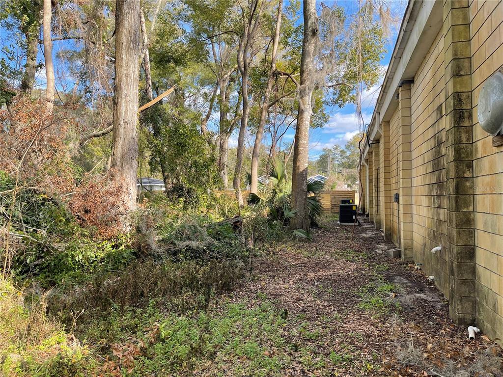 The side exterior of a building features a block wall, an air conditioning unit, and trees — lot 2 NW 135TH TERRACE, ALACHUA, FL
