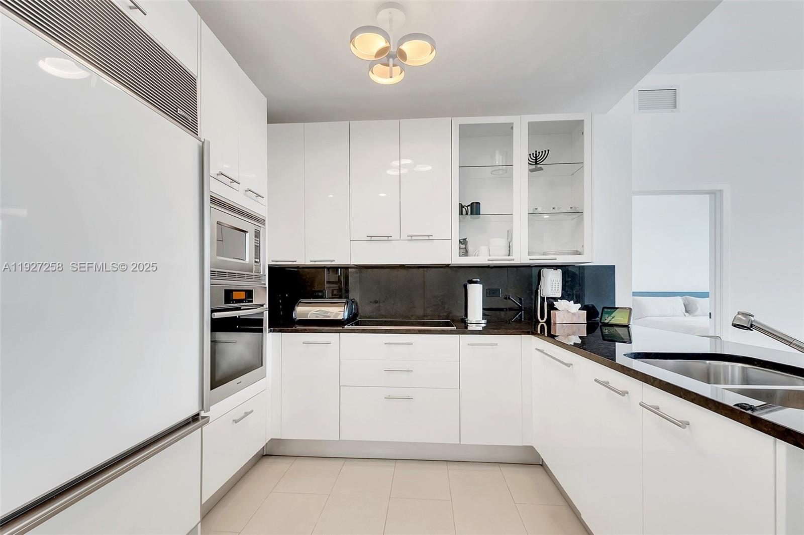 A modern kitchen features white glossy cabinets, black countertops, and stainless steel appliances — 6799 Collins Ave # 312, Miami Beach FL 33141, MIAMI BEACH, FL