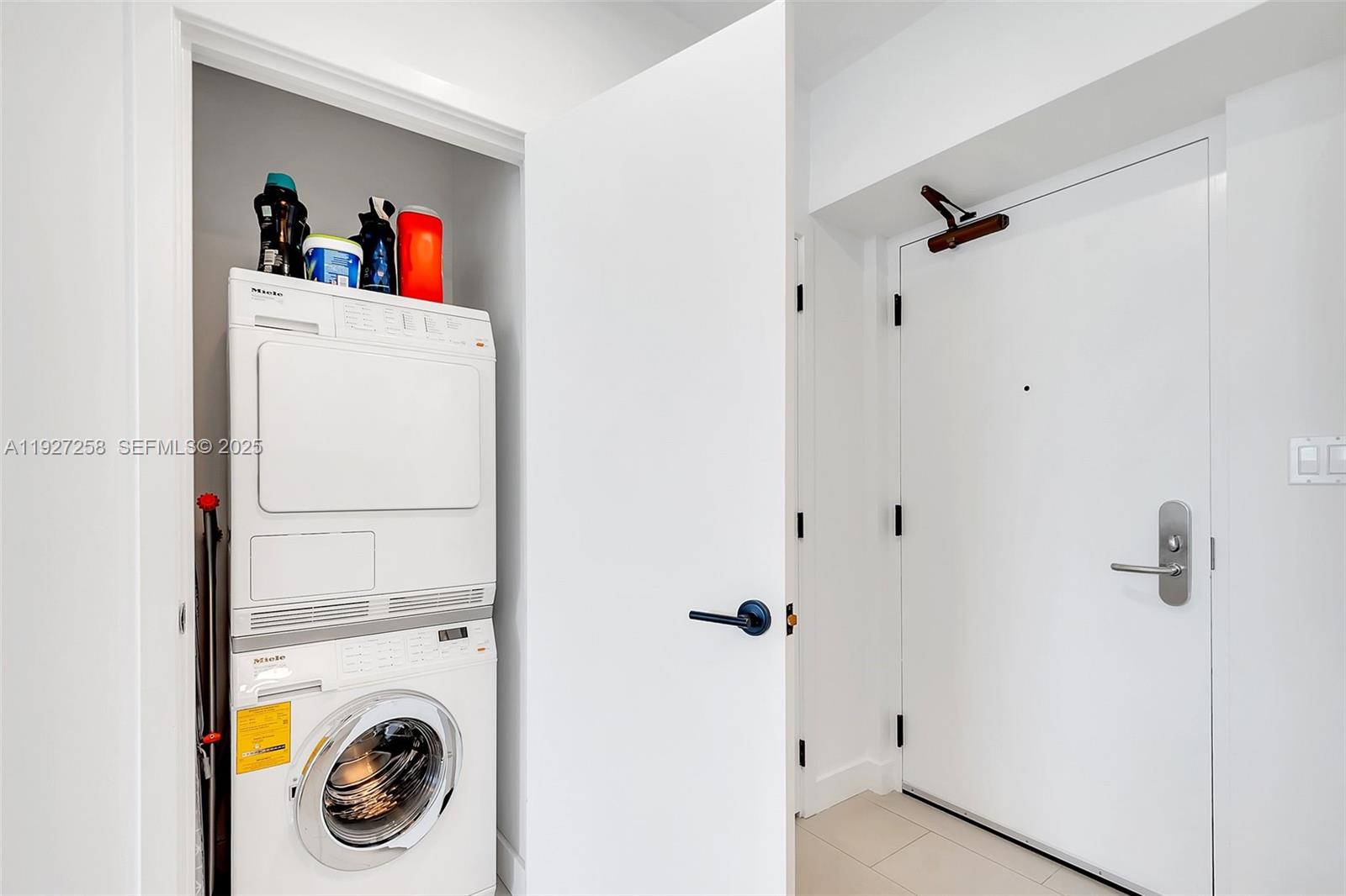 A stacked Miele washer and dryer unit sits in a closet next to a door — 6799 Collins Ave # 312, Miami Beach FL 33141, MIAMI BEACH, FL