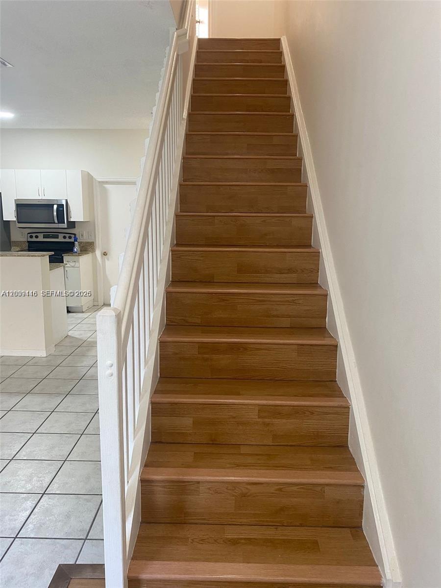 A wooden staircase with a white railing leads upward next to a tiled kitchen area — 2167 Madeira Dr # 2167, Weston FL 33327, WESTON, FL