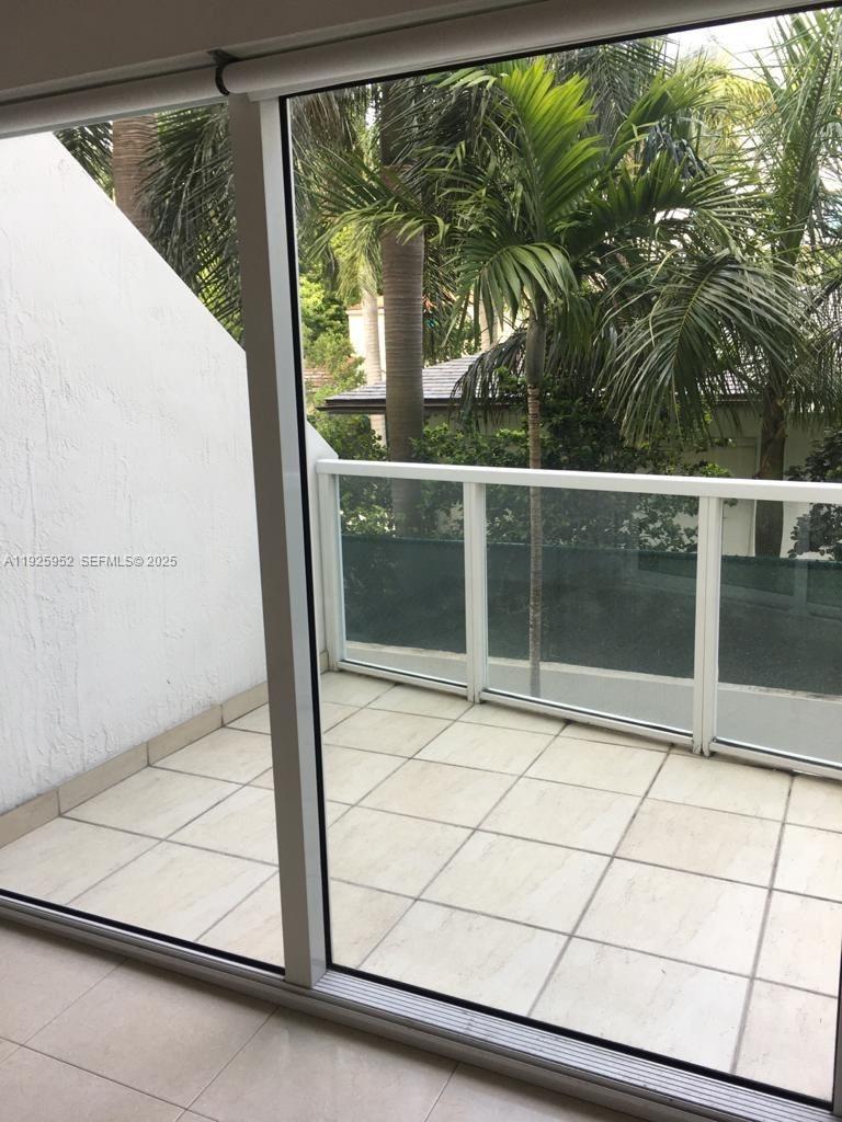 A balcony with light-colored tile flooring is viewed through large sliding glass doors — 1650 Brickell Ave # 111, Miami FL 33129, MIAMI, FL