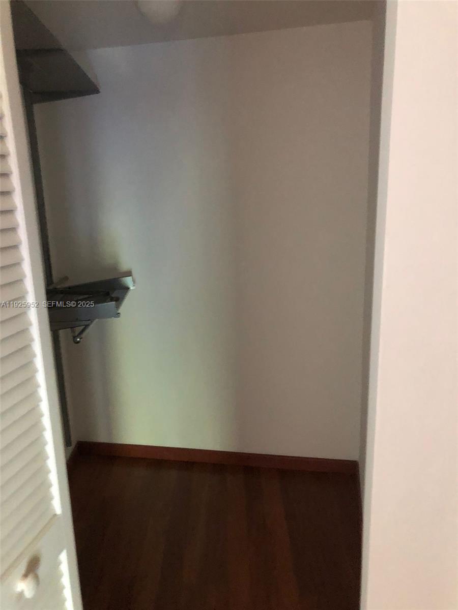 A small walk-in closet features wooden flooring and a single built-in metal shelf — 1650 Brickell Ave # 111, Miami FL 33129, MIAMI, FL