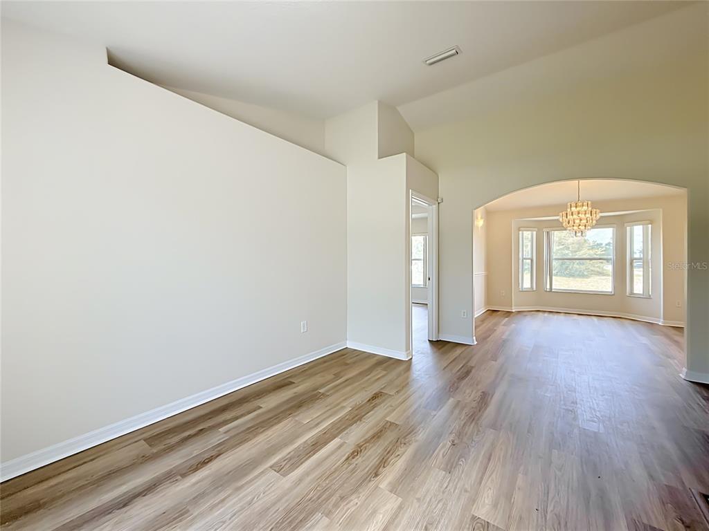 An empty room with light wood-look flooring, a vaulted ceiling, and an arched entryway — 626 MARION OAKS LANE, OCALA, FL