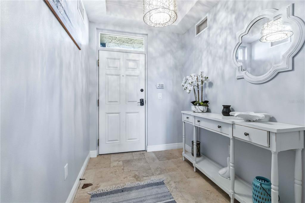A bright entryway features a white door, tile flooring, a console table, and a mirror — 4125 W END ROAD UNIT 306, COCOA BEACH, FL