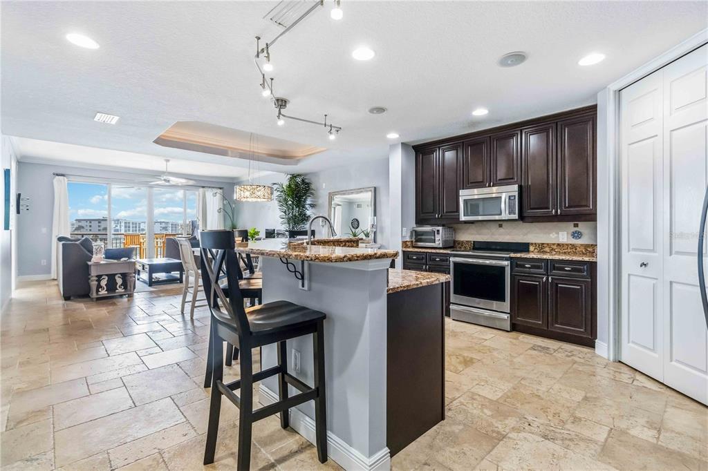 A kitchen with dark wood cabinets and granite countertops overlooks a living area with tile floors — 4125 W END ROAD UNIT 306, COCOA BEACH, FL