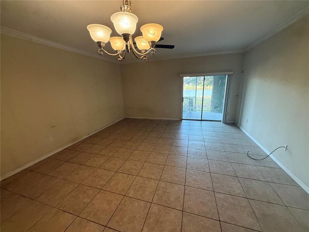 An empty room with beige tile flooring, a chandelier, and sliding glass doors to outside — 1511 HARBOUR BLUE STREET, RUSKIN, FL