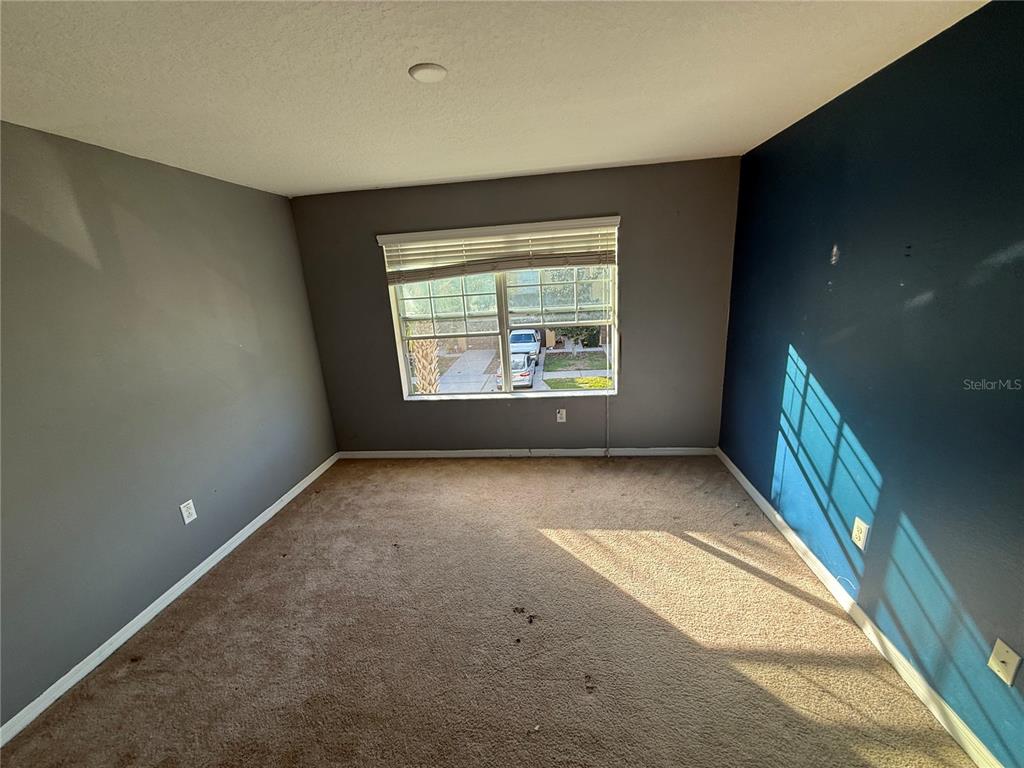 An empty bedroom features brown carpet, gray walls, one blue accent wall, and a window — 1511 HARBOUR BLUE STREET, RUSKIN, FL