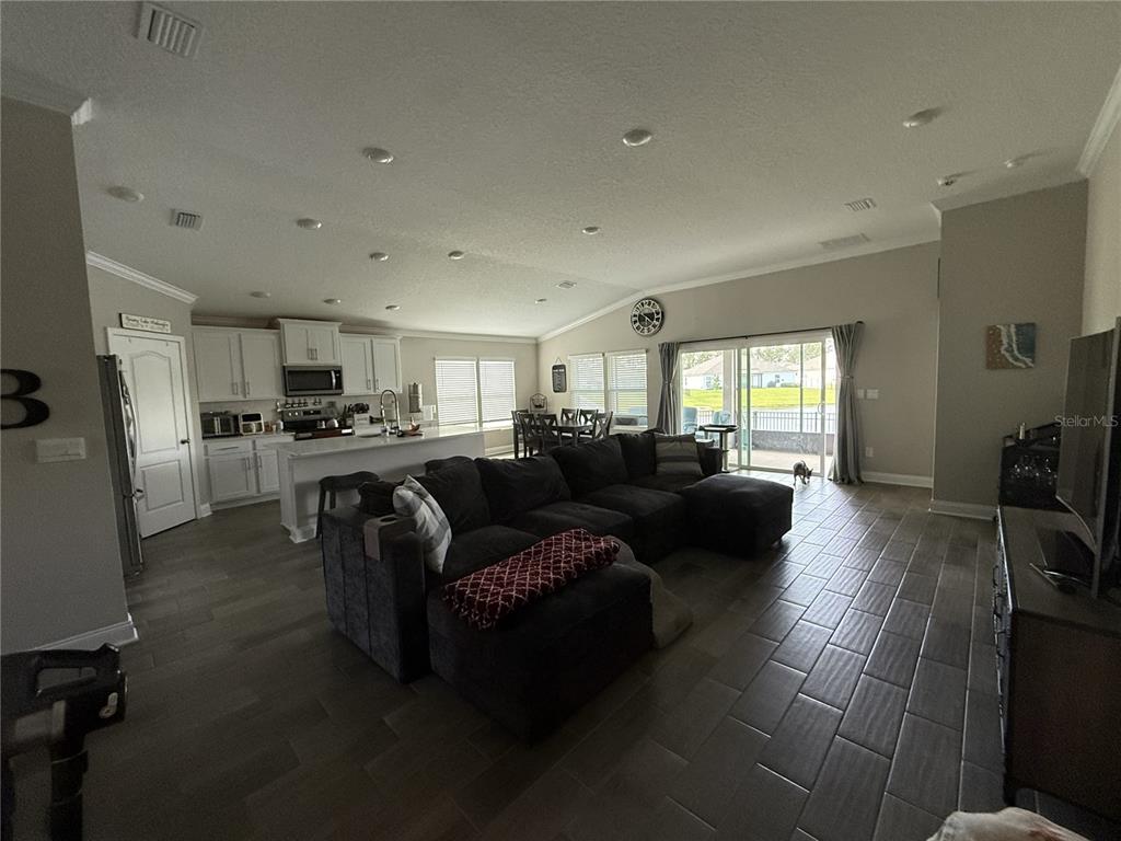 An open-concept living room and kitchen featuring dark tile floors and a large sectional sofa — 59 HULETT WOODS ROAD, PALM COAST, FL