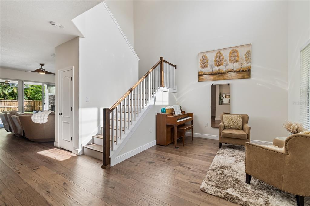 A living area with wood floors, a staircase, a piano, and two armchairs — 110 S BEVERLY AVENUE, TAMPA, FL
