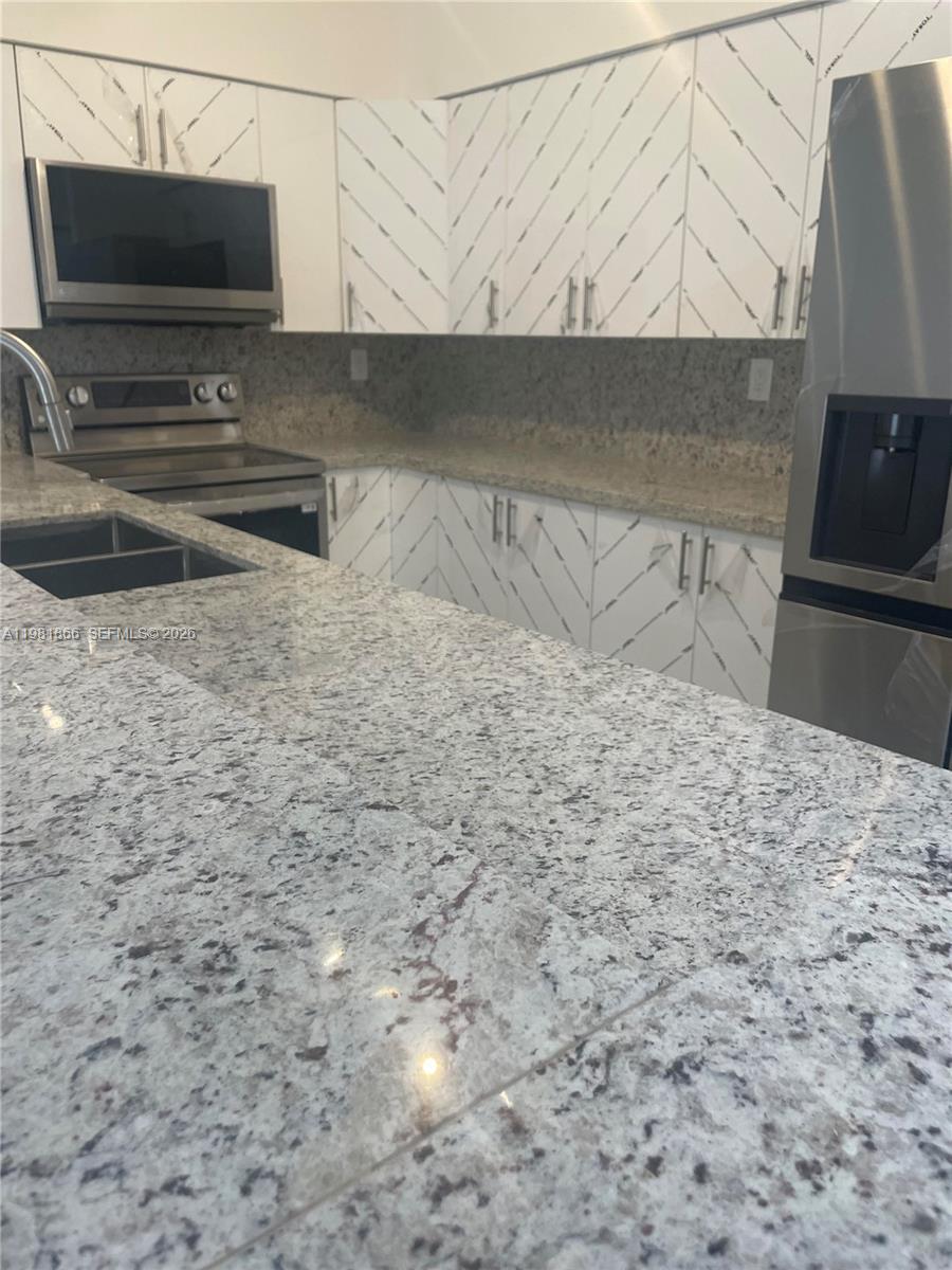 A kitchen features white cabinets with diagonal patterns, granite countertops, and stainless steel appliances — 14728 Balgowan Rd, Miami Lakes FL 33016, MIAMI LAKES, FL