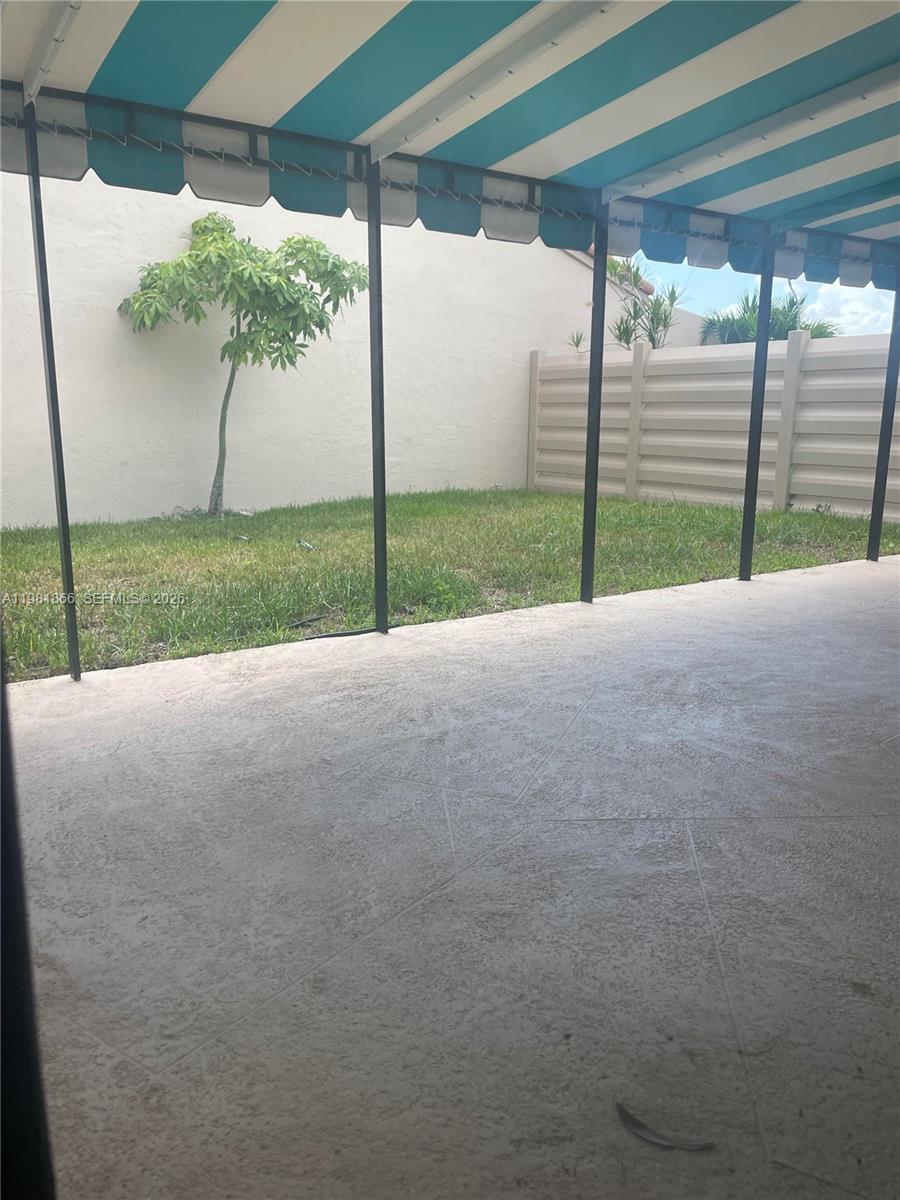 A covered patio with a striped awning overlooks a small grassy yard and fence — 14728 Balgowan Rd, Miami Lakes FL 33016, MIAMI LAKES, FL