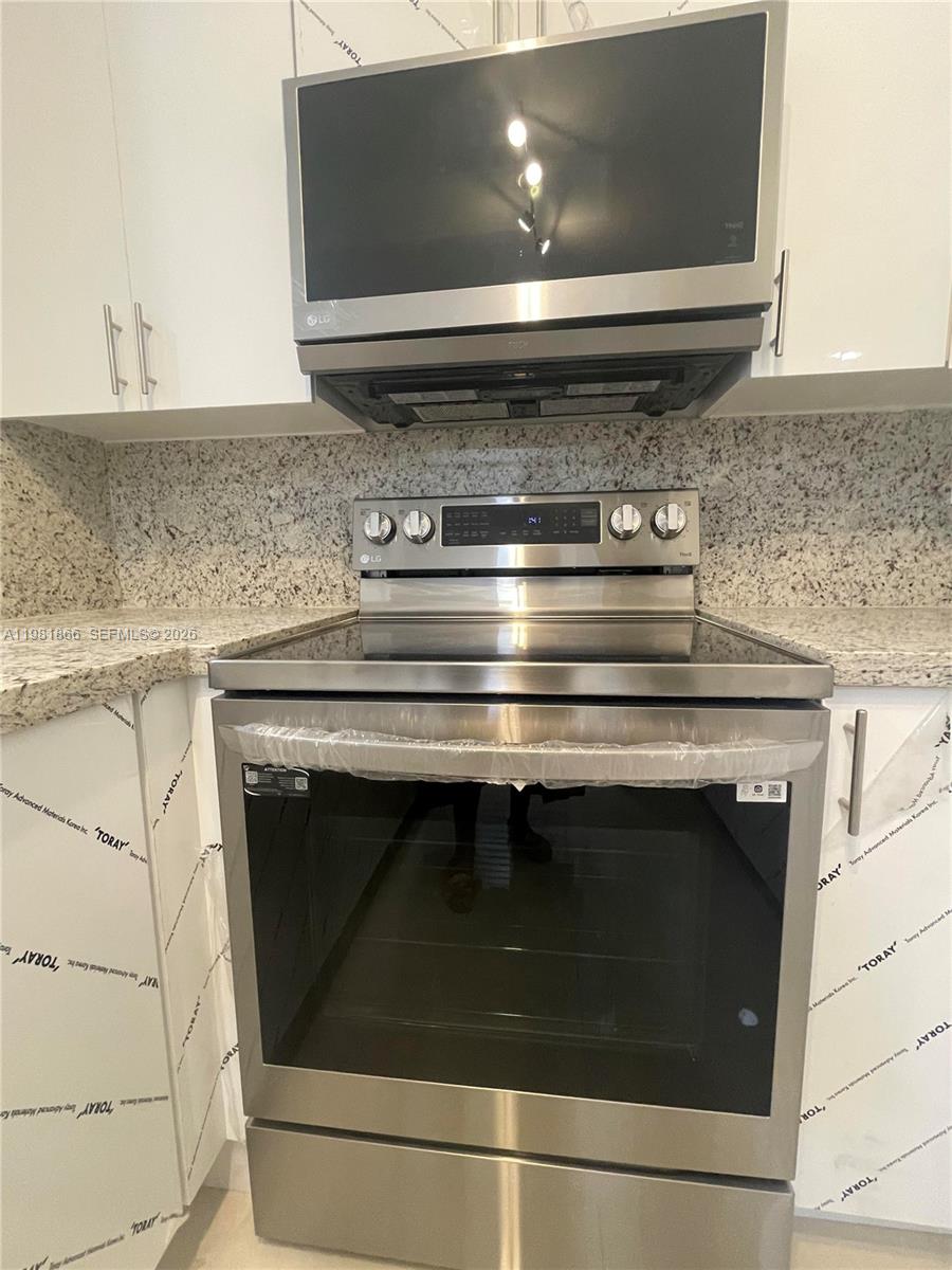 A stainless steel oven and microwave are installed in a kitchen with white cabinets — 14728 Balgowan Rd, Miami Lakes FL 33016, MIAMI LAKES, FL